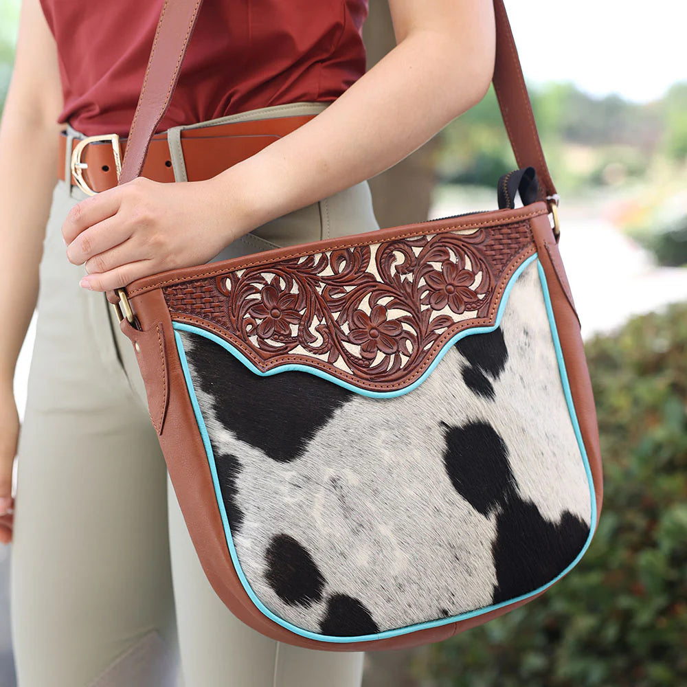 Person holding a brown leather and cowhide patterned handbag with decorative elements.