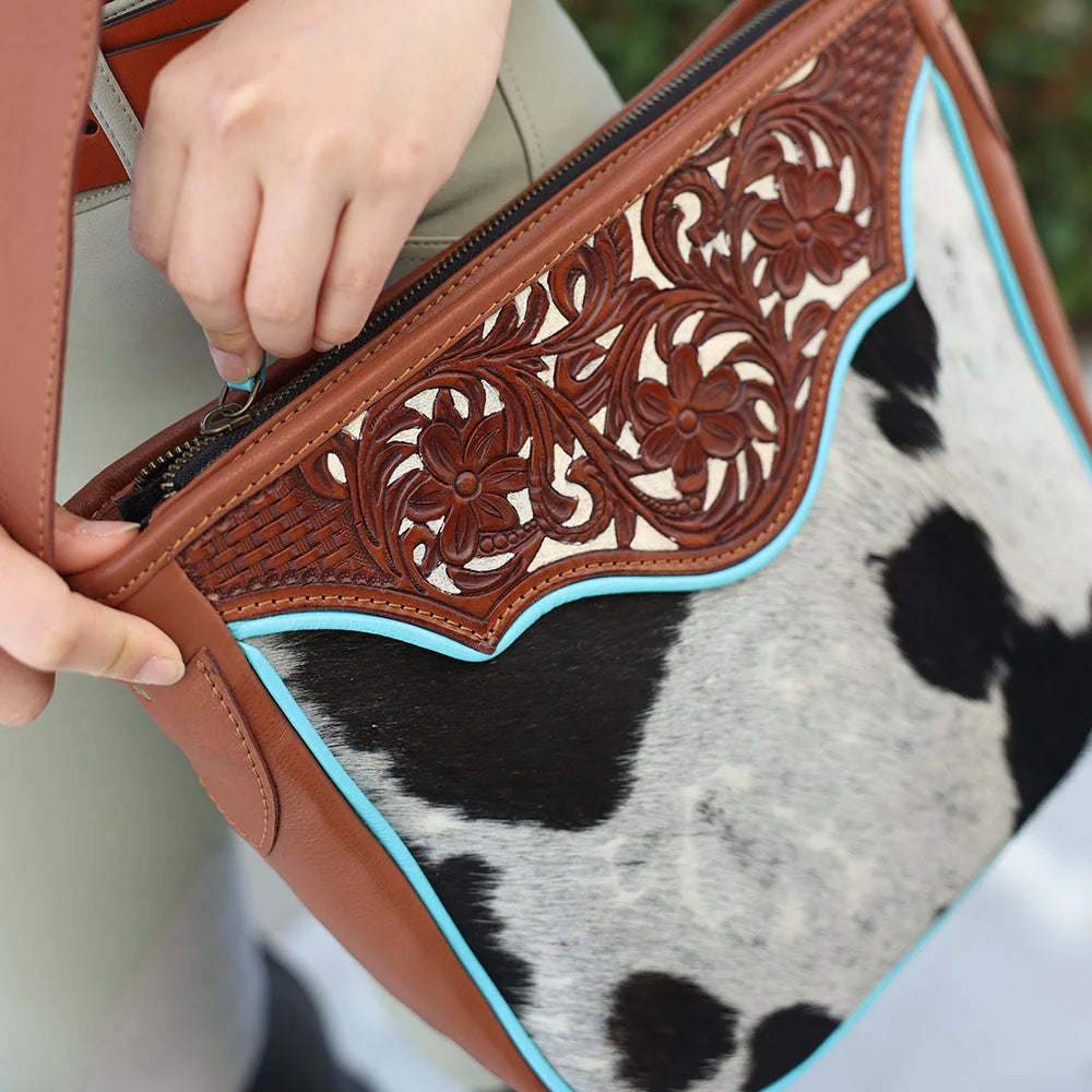 Close-up of a handbag with intricate leatherwork and cowhide pattern.