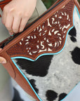 Close-up of a handbag with intricate leatherwork and cowhide pattern.