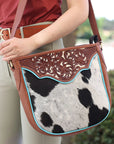 Person holding a brown leather and cowhide patterned handbag with decorative elements.
