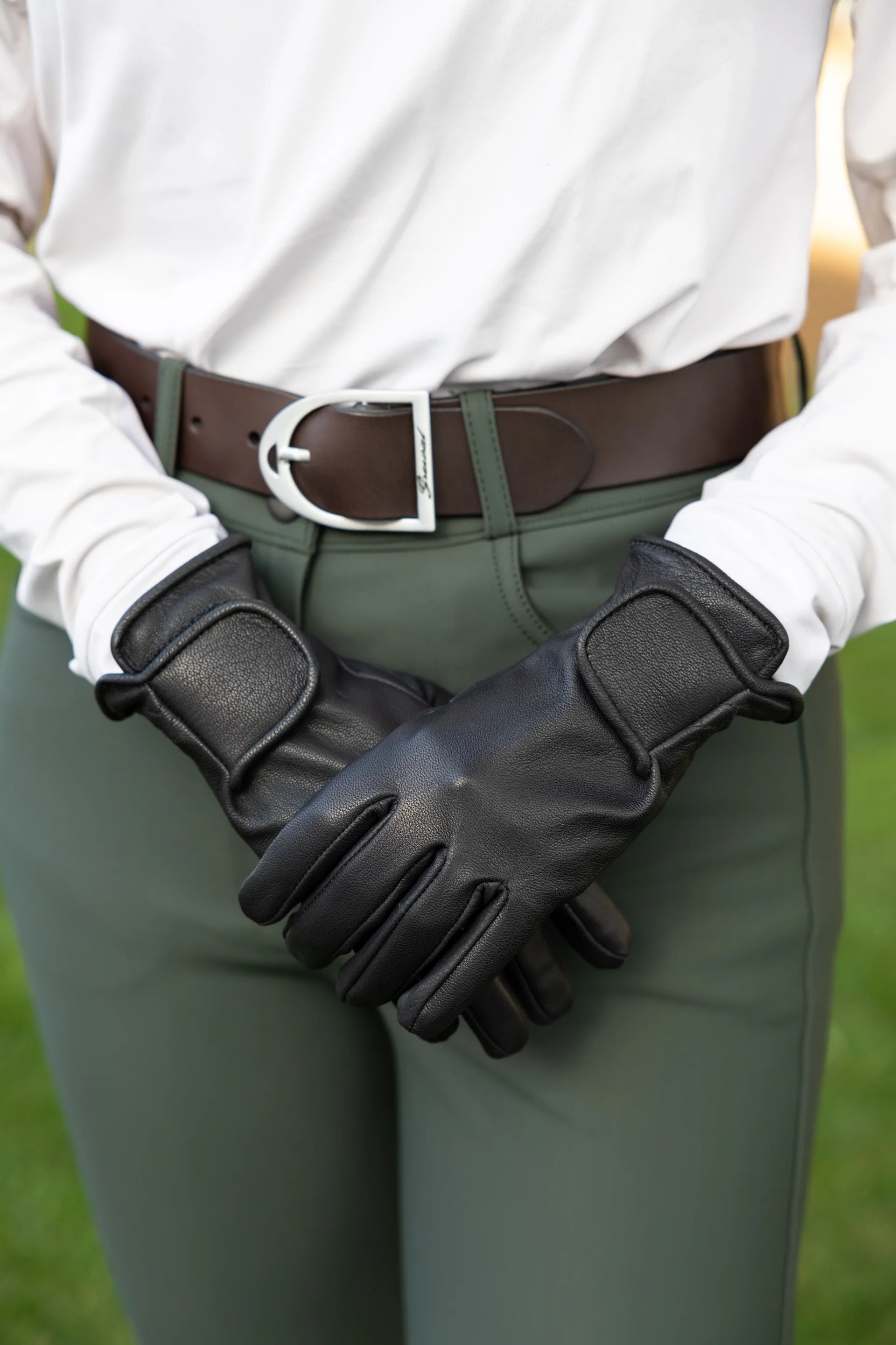 Person wearing black leather gloves with a blurred green background