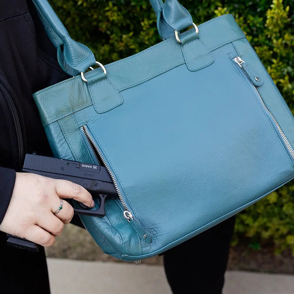 Person holding a teal handbag with a gun inside, blurred background