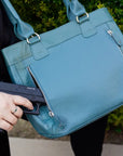 Person holding a teal handbag with a gun inside, blurred background