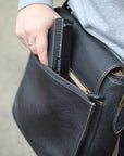 Person placing a phone into a black leather bag.