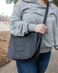 Person wearing a gray sweatshirt and holding a dark gray leather bag outdoors.
