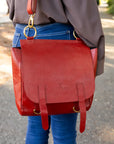 Red leather bag with gold hardware worn by a person on a blurred outdoor background