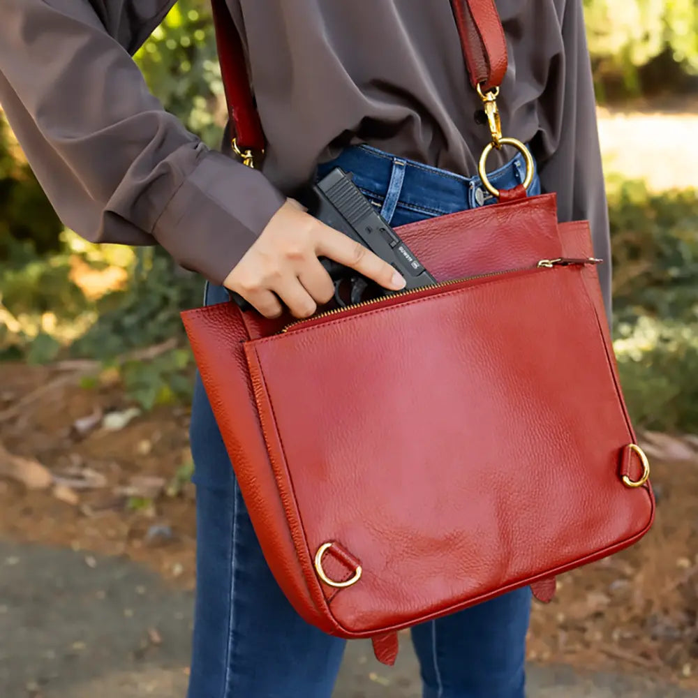 Person holding a red handbag with a gun inside, outdoors.