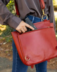 Person holding a red handbag with a gun inside, outdoors.