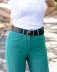 Teal riding pants with a black belt and white shirt on a blurred background