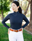 Woman wearing a navy long-sleeve top and white pants with a brown belt, standing outdoors.