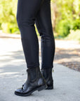 Person wearing black riding boots and pants on a blurred outdoor background