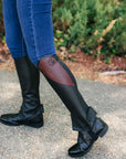 Person wearing black riding boots with red accents on a paved surface.