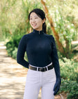 Woman wearing a dark blue long-sleeve top and white pants outdoors.