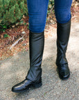 Black riding boots worn with blue jeans on a pavement background