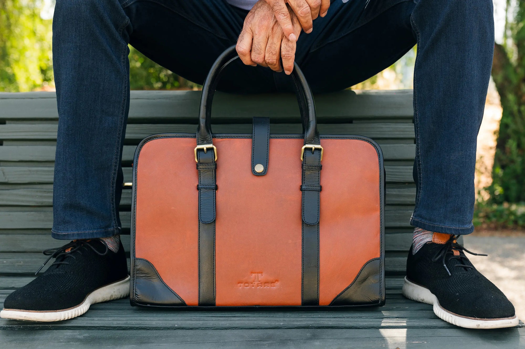 Person sitting on a bench with an orange and black leather briefcase in front of them.