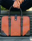 Person sitting on a bench with an orange and black leather briefcase in front of them.