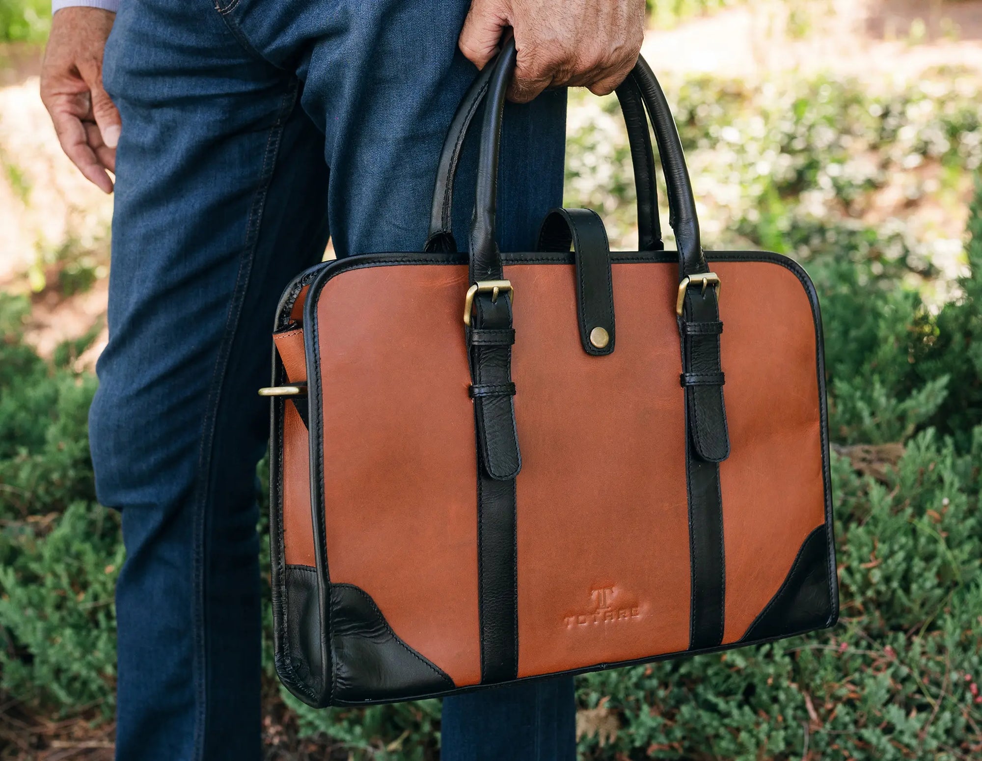 Brown leather briefcase with black accents held by a person outdoors.