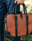 Brown leather briefcase with black accents held by a person outdoors.