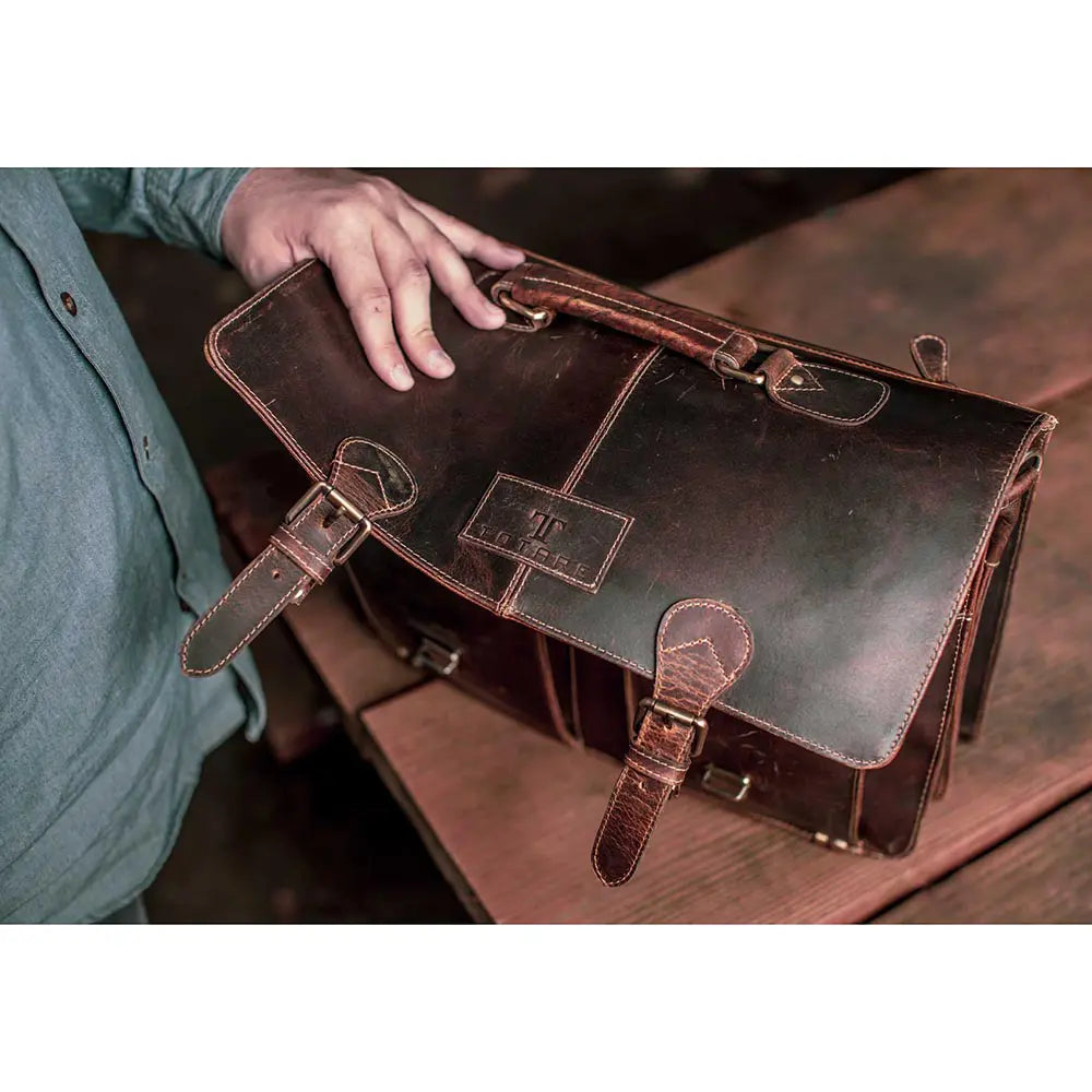Brown leather satchel bag held by a person on a wooden surface
