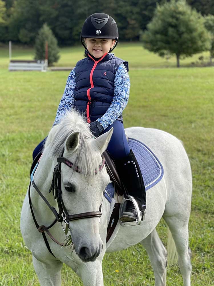 Young rider wearing Lewis Children's Half Chaps while riding white pony