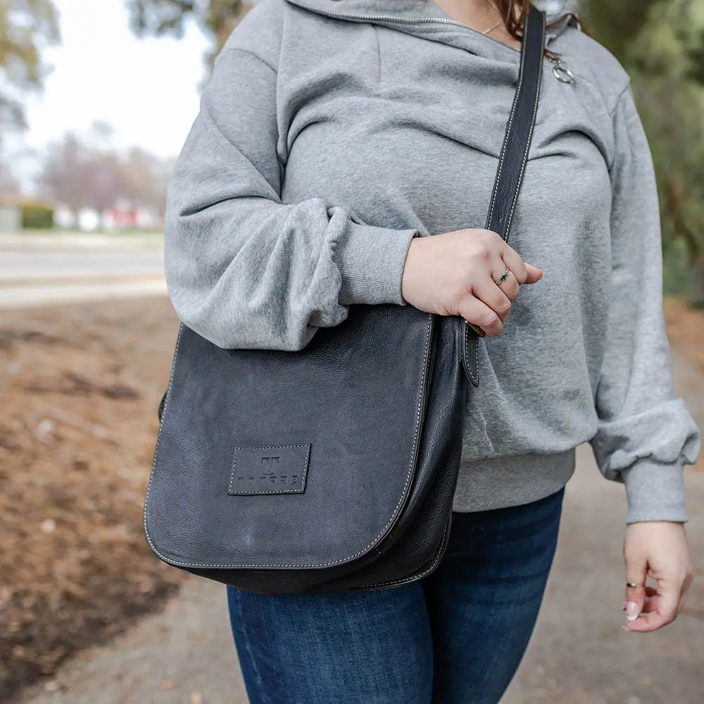 Person wearing a gray sweatshirt and holding a dark gray leather bag outdoors.