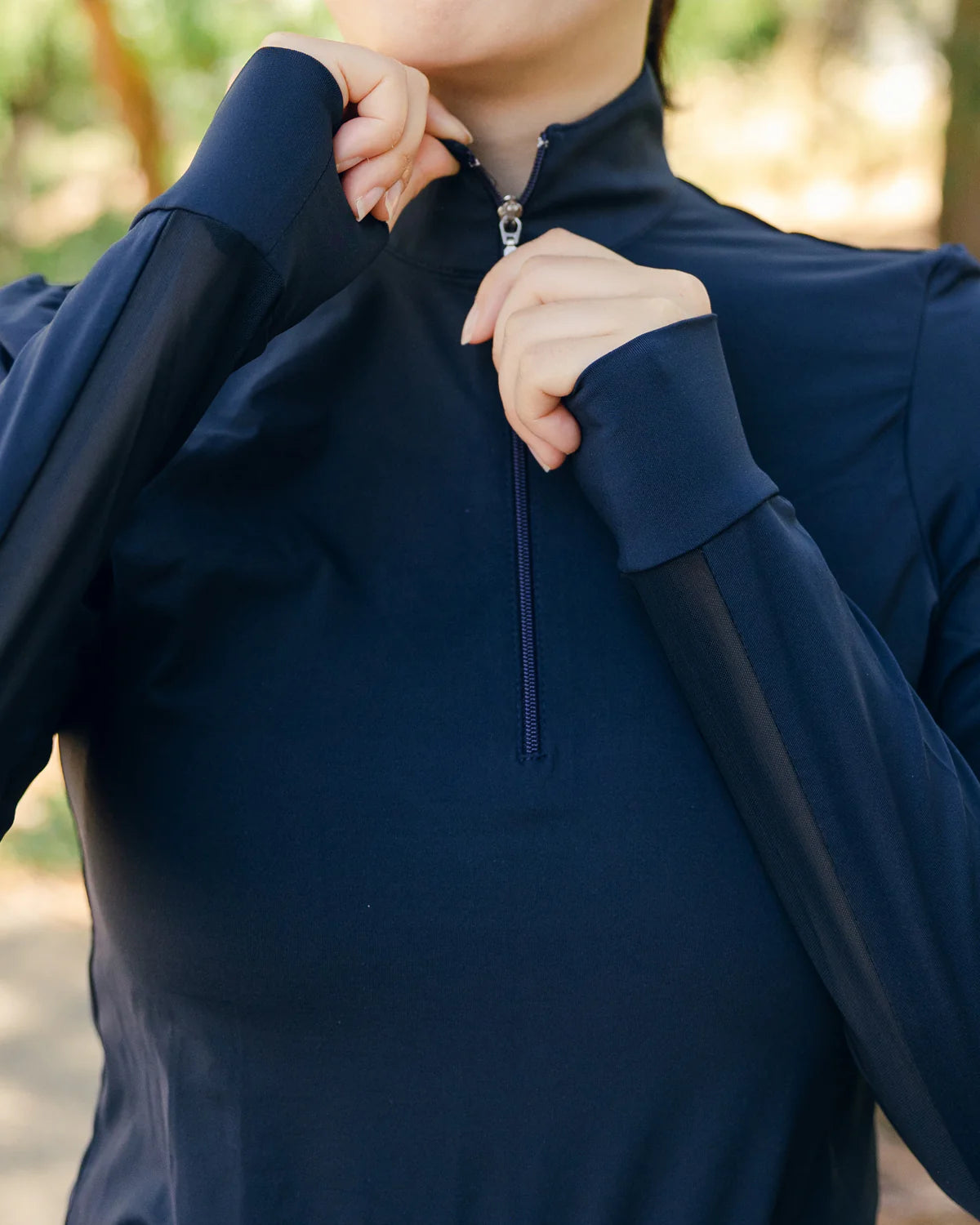 Person wearing a navy blue long-sleeve shirt with a zipper, outdoors.