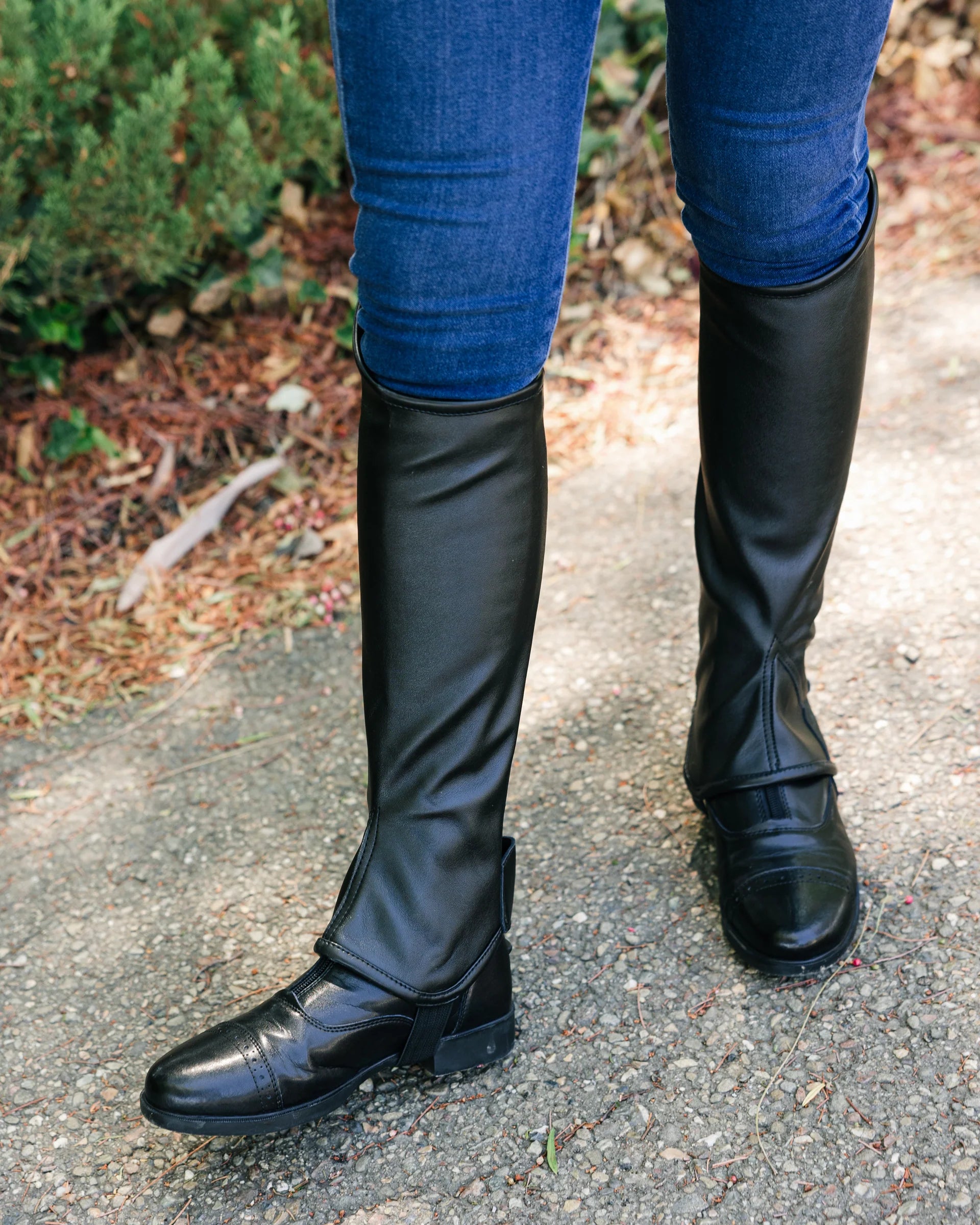 Black riding boots worn with blue jeans on a pavement background